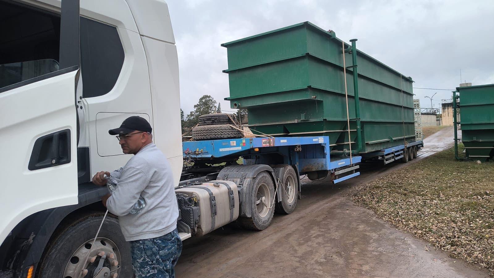 Tanques industriales verdes cargados sobre carretón, con el chofer junto a la unidad