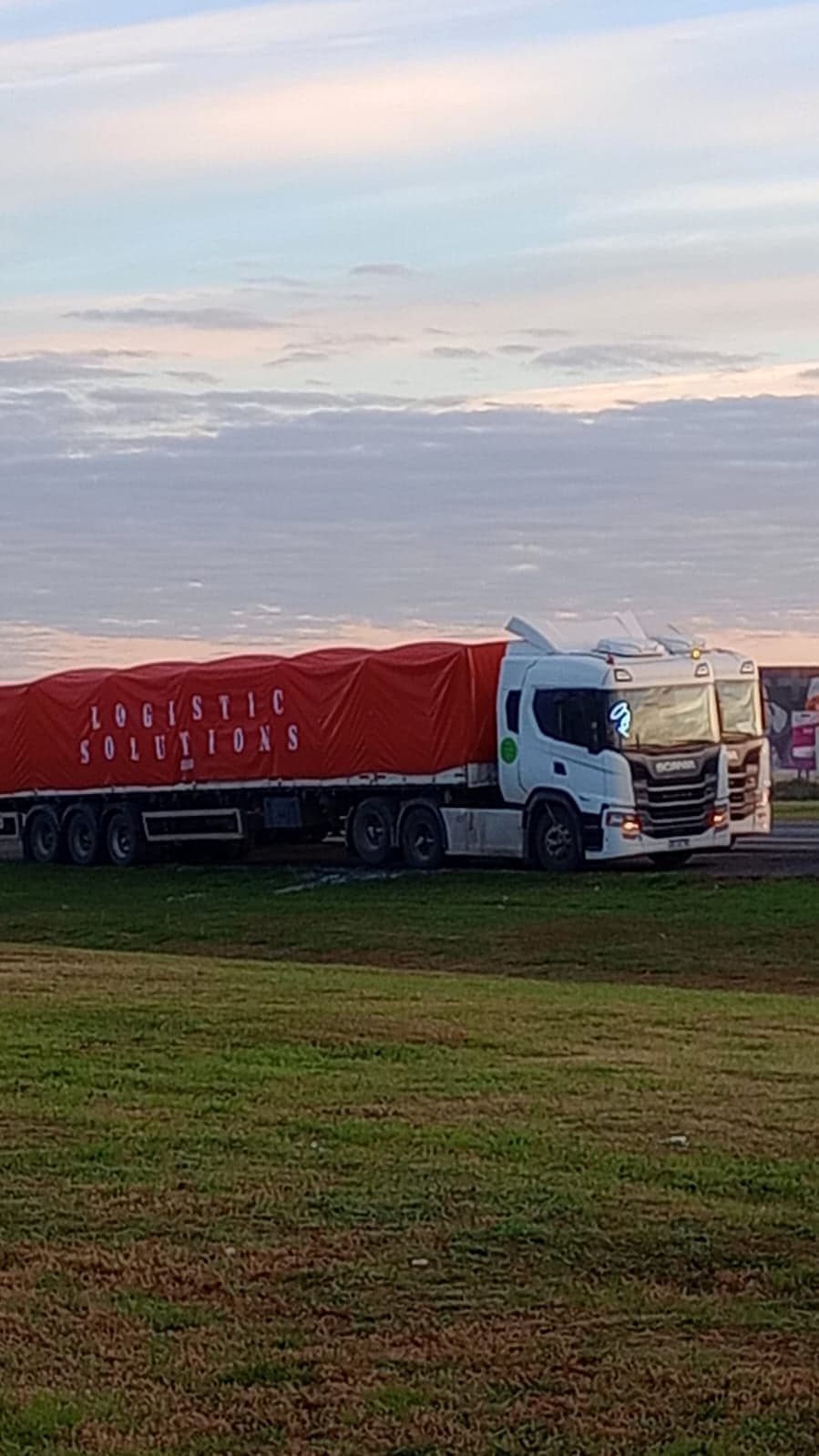 Tractor Scania con semirremolque lonado en rojo con la leyenda Logistic Solutions, al amanecer
