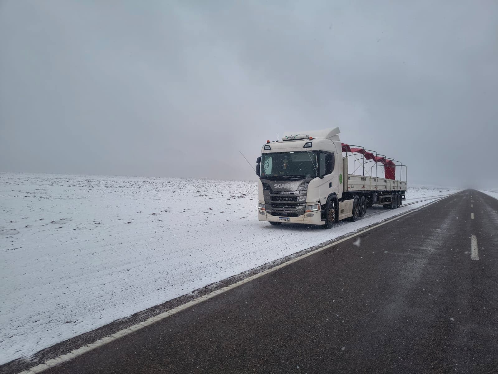 Tractor Scania con semirremolque circulando por una ruta de altura cubierta de nieve